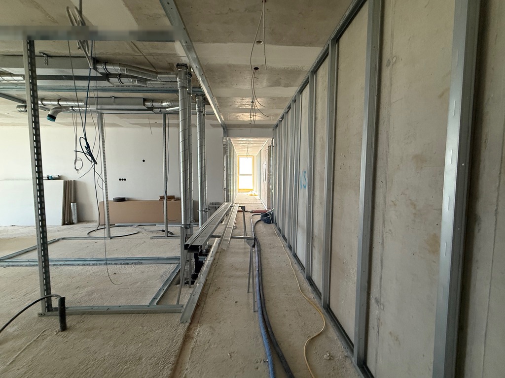 Flur mit Metallständerwerk vor der Betonwand, links Installationen unter der Decke